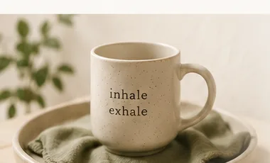 A speckled mug printed with the words inhale, exhale resting on a plate with a sage linen napkin